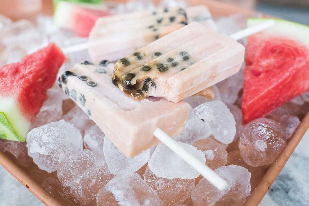 Two popsicles with visible passion fruit seeds rest on ice, surrounded by juicy watermelon slices, adding a refreshing touch perfect for your favorite watermelon recipes.