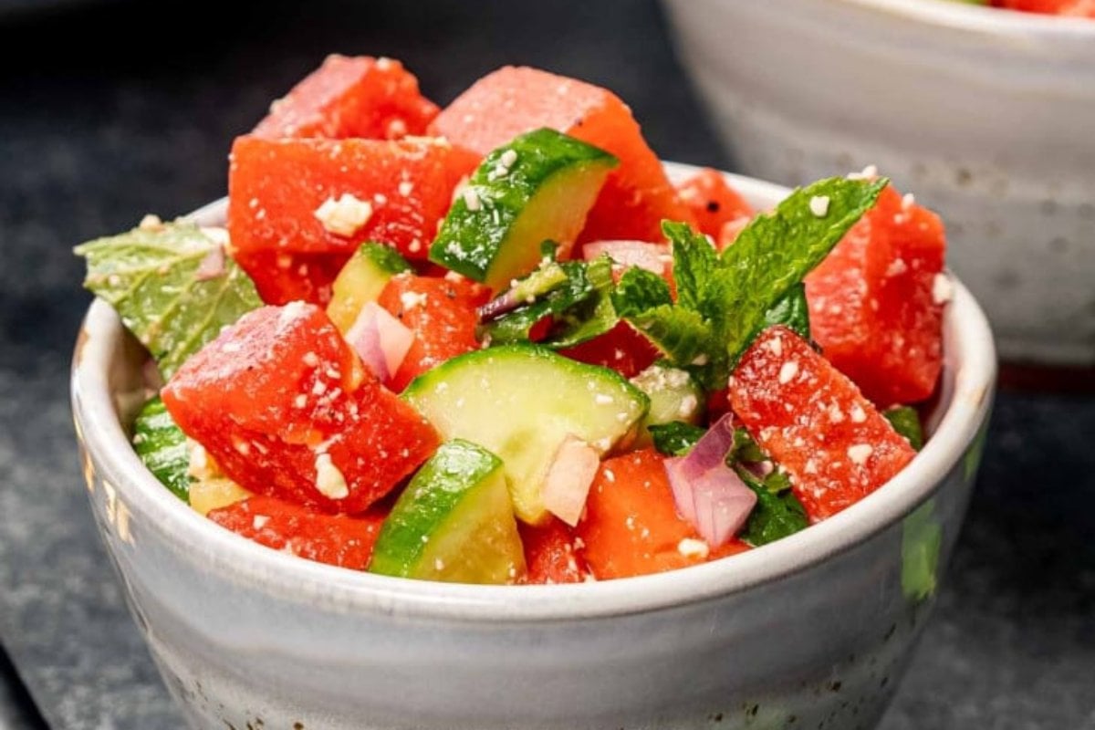 A bowl of watermelon salad with cucumber, red onion, mint leaves, and crumbled cheese is a perfect addition to your favorite watermelon recipes.