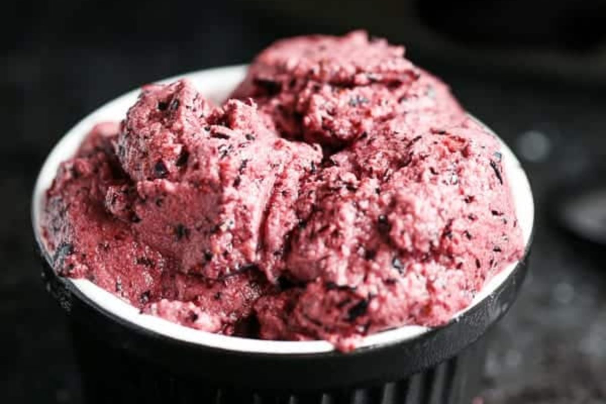A bowl filled with a heaping serving of dark pink ice cream with visible chunks of fruit, perfect for fans of blueberry recipes.