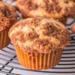 Close-up of freshly baked snickerdoodle muffins with crumbly, golden-brown tops cooling on a round wire rack.