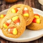 A plate of round, tan candy corn peanut butter cookies on a wooden surface next to a checkered cloth.