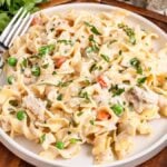 A plate of homemade tuna helper with pieces of tuna, green peas, and carrots, garnished with chopped parsley, with a fork on the left side of the plate.