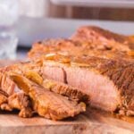 Sliced, slow cooker beef brisket on a wooden cutting board with visible grill marks and a slightly crispy outer layer.