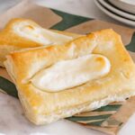 Two Starbucks copycat cheese Danish pastries with a creamy filling rest on a leaf-patterned paper.