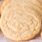 A close-up view of several vanilla cookies placed on a sheet of white parchment paper.