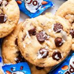 Almond Joy chocolate chip cookies scattered among blue almond candy wrappers.