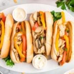 A platter of four chicken Philly sandwiches with bell peppers and topping dips, garnished with fresh cilantro, viewed from above.