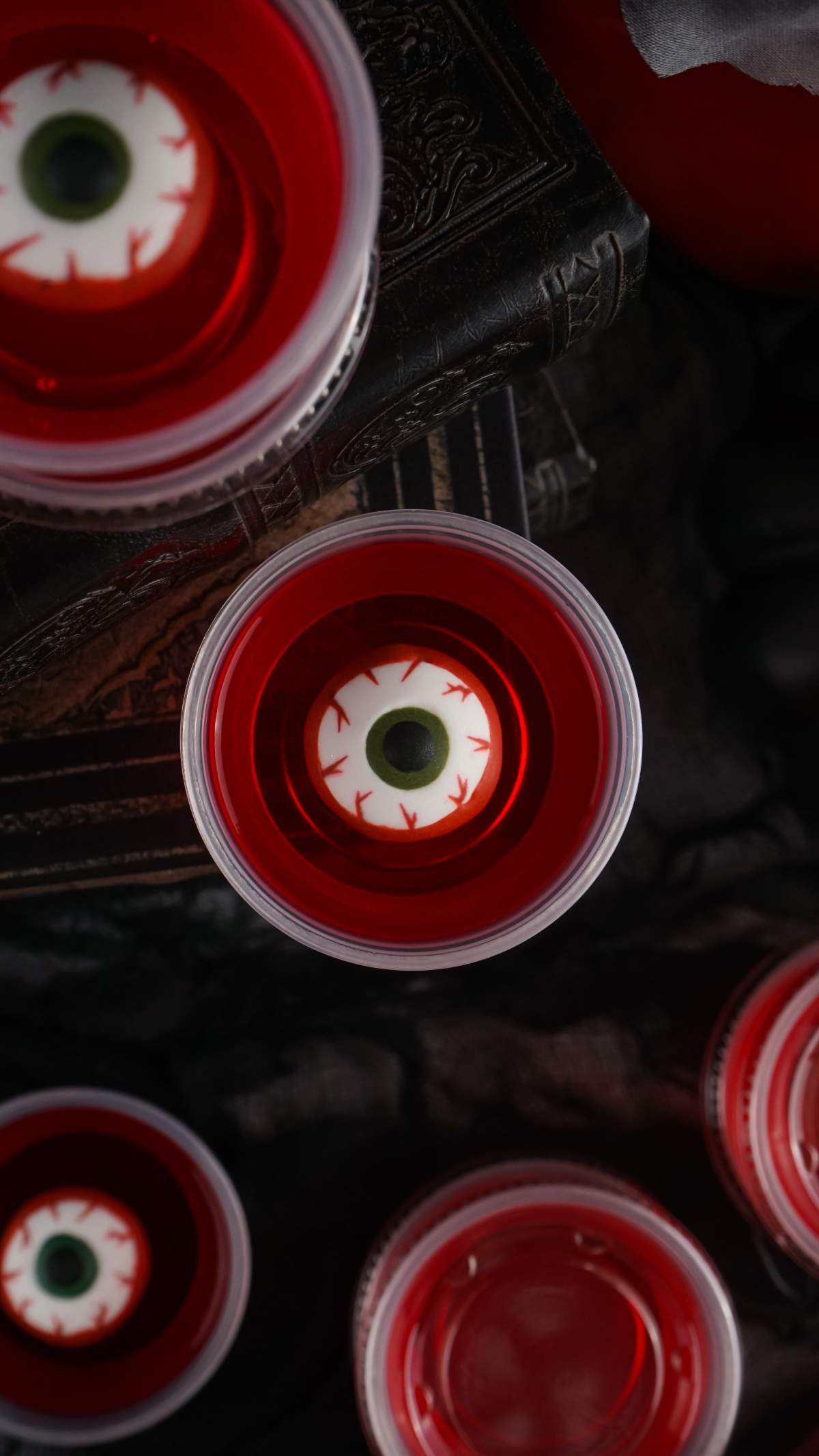 Close-up of Halloween eyeball jello shots in plastic cups placed on a textured dark surface.