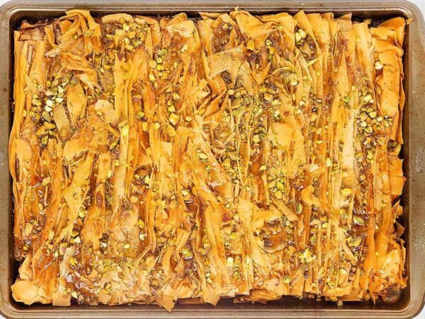 A tray of golden, flaky baklava crinkle topped with chopped pistachios, viewed from above.
