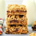 A stack of three carmelitas bars sits surrounded by two milk bottles and a colorful plaid cloth.