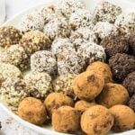 A plate of delightful homemade chocolate truffles, featuring an assortment coated with nuts, cocoa powder, and chocolate sprinkles.