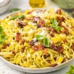 A plate of spaghetti corn carbonara mixed with bacon, and basil, then topped with grated cheese.