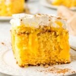 A slice of moist yellow eggnog poke cake with a creamy filling and whipped topping sits elegantly on a white plate.