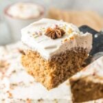 A slice of frosted eggnog tres leches cake is being lifted with a spatula. The cake is topped with rich cream and garnished with star anise, promising a delightful blend of flavors.