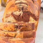 A marble loaf cake, partially sliced, sits on a white surface beside a small bowl of raspberries, a cup of coffee, and a glass of orange juice.