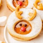 Biscoff reindeer Linzer cookies, adorned with red candy noses, chocolate eyes, and biscuit antlers, create a whimsical holiday treat on the plate.