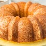 A rum bundt cake on a plate with a light glaze sits enticingly next to a cup of coffee and a fork.