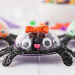 Candy spiders with colorful bows and googly eyes adorn the DIY Halloween spider candy holder, creating a festive table centerpiece.