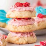 A stack of cookies with pink frosting and dried strawberries sits amidst a delightful array of sour cream cookies adorned with blue and pink frosting.