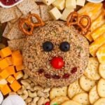 A delightful Christmas reindeer cheese ball takes center stage, surrounded by an array of crackers, cheese cubes, nuts, grapes, and pickles on a rustic wooden board.