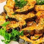 A plate of perfectly roasted acorn squash slices, elegantly garnished with fresh parsley, rests on a woven placemat.