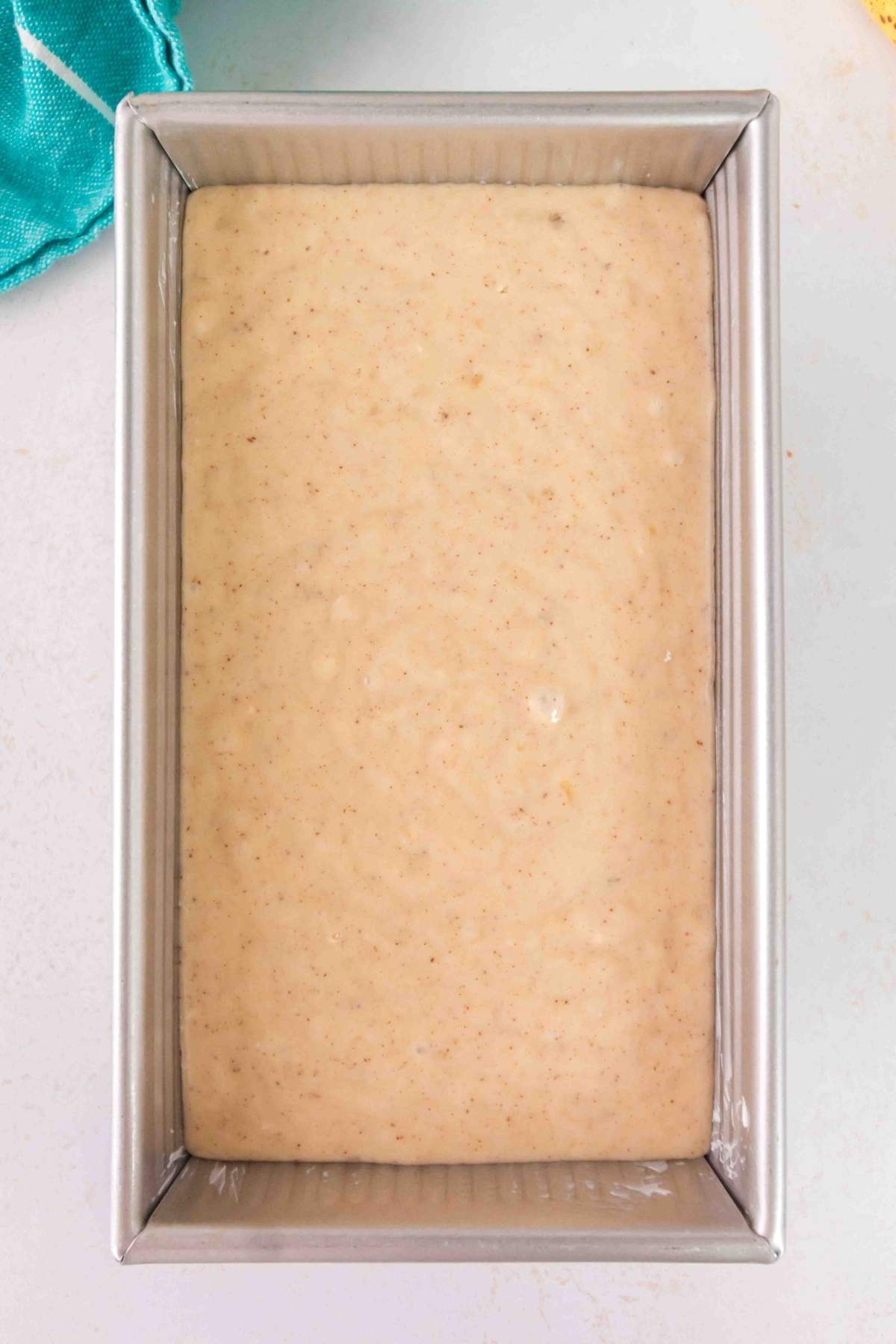The batter for a delicious brown butter banana bread is nestled in a rectangular metal baking pan, ready to be baked.