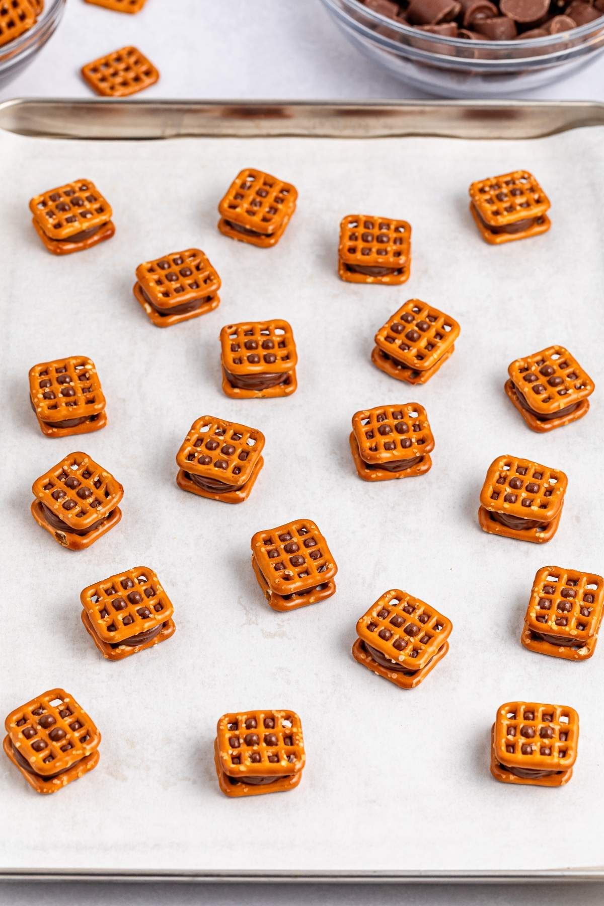 Several chocolate-filled pretzel sandwiches, resembling delightful Christmas Rolo pretzel bites, are arranged on a metal baking tray.