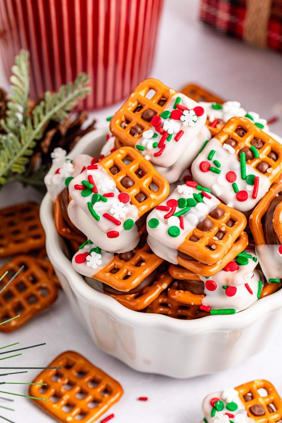 A bowl of Christmas Rolo pretzel sandwiches topped with white frosting and festive red, green, and white sprinkles.