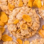 Close-up of round, crumbly cornflake cookies with crispy flakes on top, scattered on a white surface.