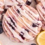 A close-up of lemon blueberry cookies with white icing, nestled among fresh blueberries and slices of lemon.