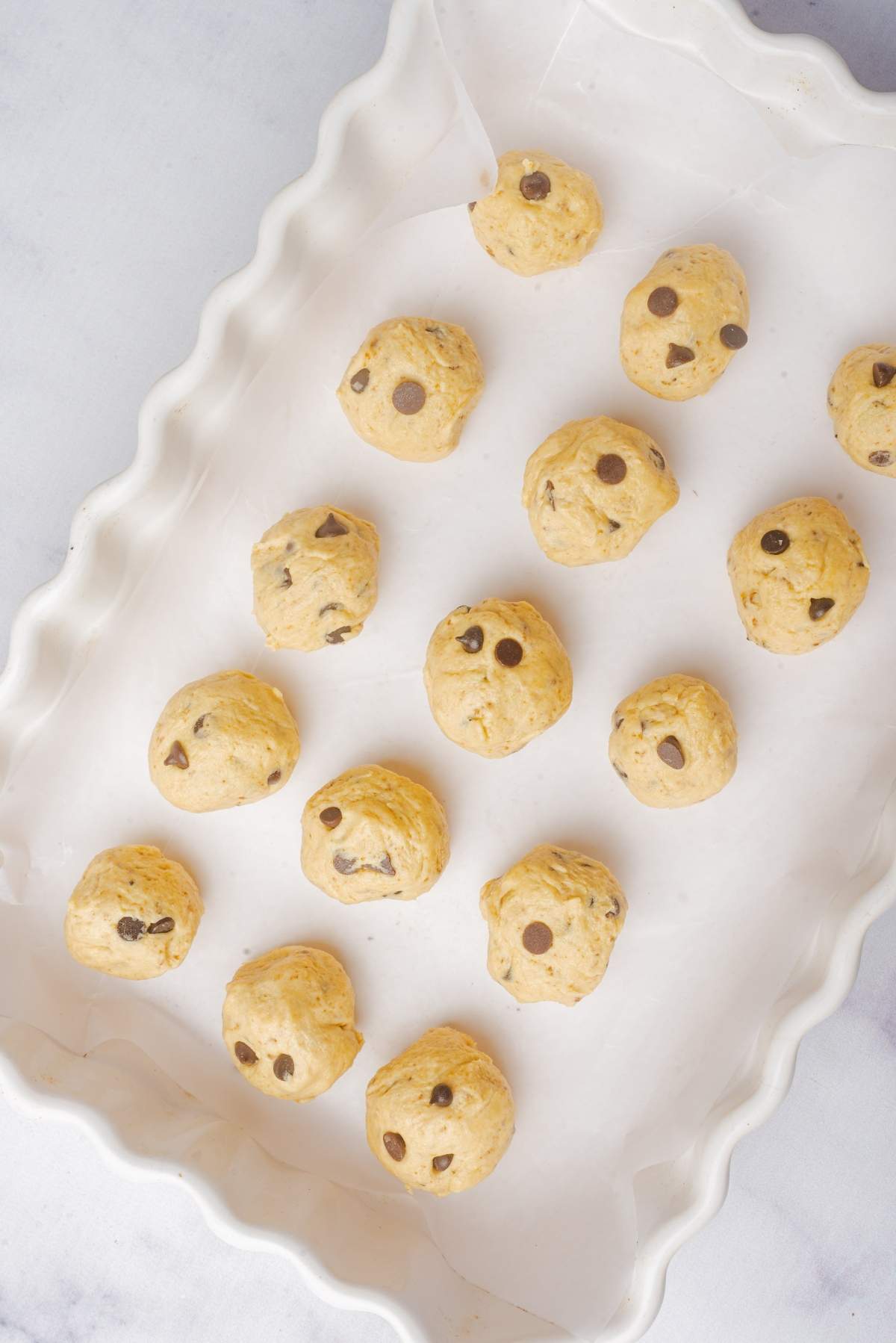 No churn cookie dough ice cream awaits as raw chocolate chip cookie dough balls rest on a parchment-lined baking tray.