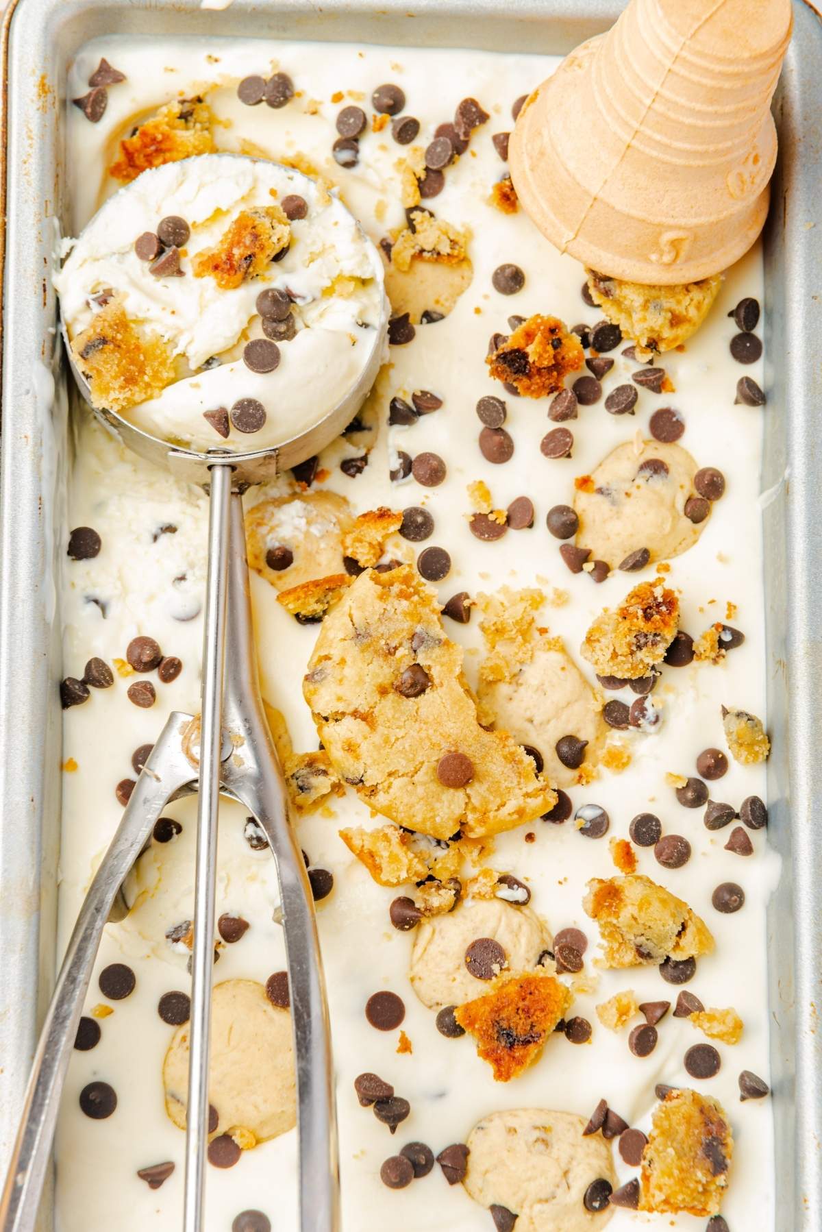 Enjoy a tray of no churn cookie dough ice cream swirled with chocolate chip cookies and sprinkled with rich chocolate chips, paired perfectly with an ice cream scoop and an empty cone for serving.
