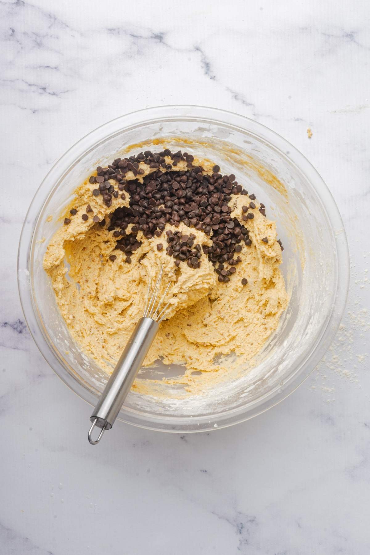 A bowl of no churn cookie dough ice cream with chocolate chips and a whisk sits elegantly on a marble surface.