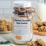 A jar of oatmeal chocolate chip cookie mix sits front and center, its recipe label offering delicious promise. Freshly baked cookies spill onto a plate nearby, with a bottle of milk waiting in the background.