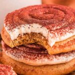 A stack of tiramisu cookies with icing and cocoa, one cookie has a bite taken out.