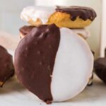 A delightful selection of black and white cookies, adorned with luscious chocolate and vanilla icing, rests invitingly on a pristine white surface.