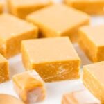 Close-up of several pieces of caramel fudge candy, some wrapped and others unwrapped, arranged on a light surface, reminiscent of a homemade caramel fudge recipe.