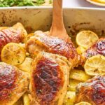 Greek lemon chicken thighs with lemon slices on top, served over sliced potatoes in a baking dish.
