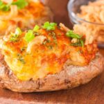 Air fryer twice-baked French onion baked potato topped with melted cheese, green onions, and crispy onions on a wooden surface.