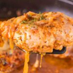 Close-up of a spatula holding a piece of French onion chicken, cooked to perfection in a rich sauce with herbs sprinkled on top, hovering above the pan.