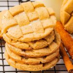 A stack of cinnamon lattice cookies rests on a cooling rack, with fragrant cinnamon sticks scattered nearby.