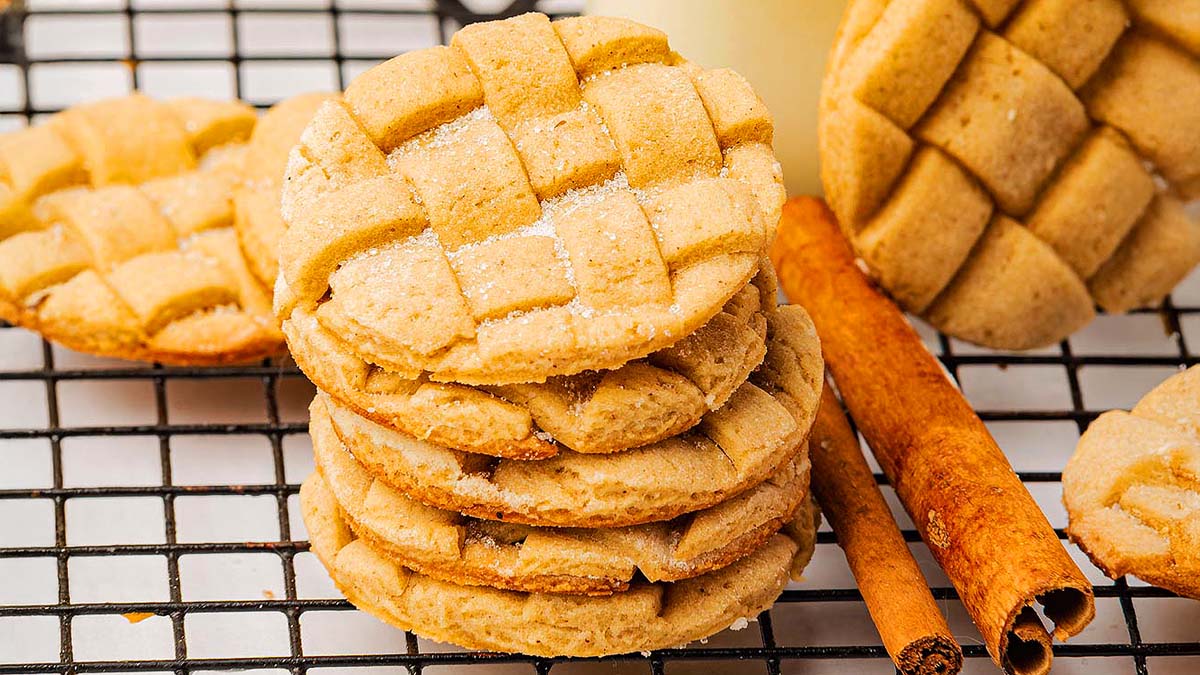 A stack of lattice-patterned cookies on a cooling rack with cinnamon sticks beside them.