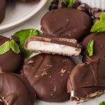 Homemade York peppermint patties glisten on the white surface, surrounded by fresh mint leaves, adding a touch of nature's charm.