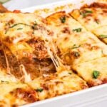A baking dish of cheese-covered ravioli lasagna, with a slice being lifted out to reveal delightful layers of pasta pillows, savory meat, and rich sauce.
