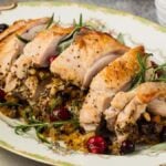 Sliced stuffed turkey breast with a delightful blend of herbs and nuts, garnished with cranberries and rosemary, elegantly served on a floral-patterned platter.