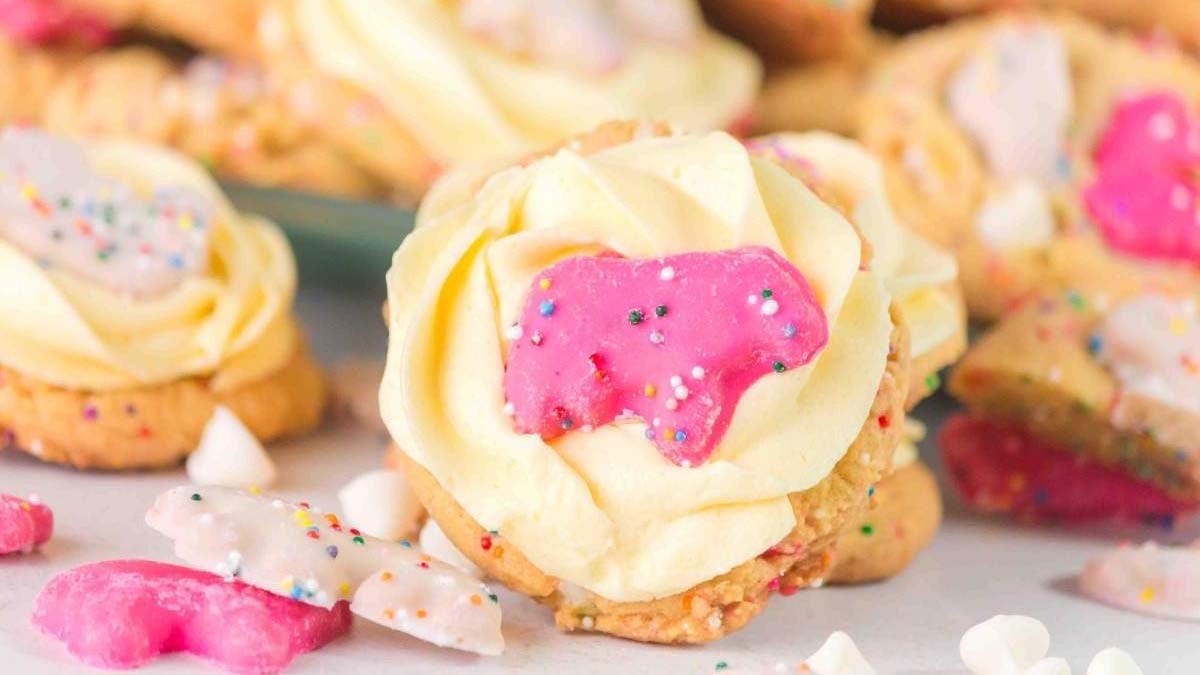 Cookies topped with white and pink animal-shaped frosted cookies and sprinkles, with a creamy yellow frosting layer underneath.