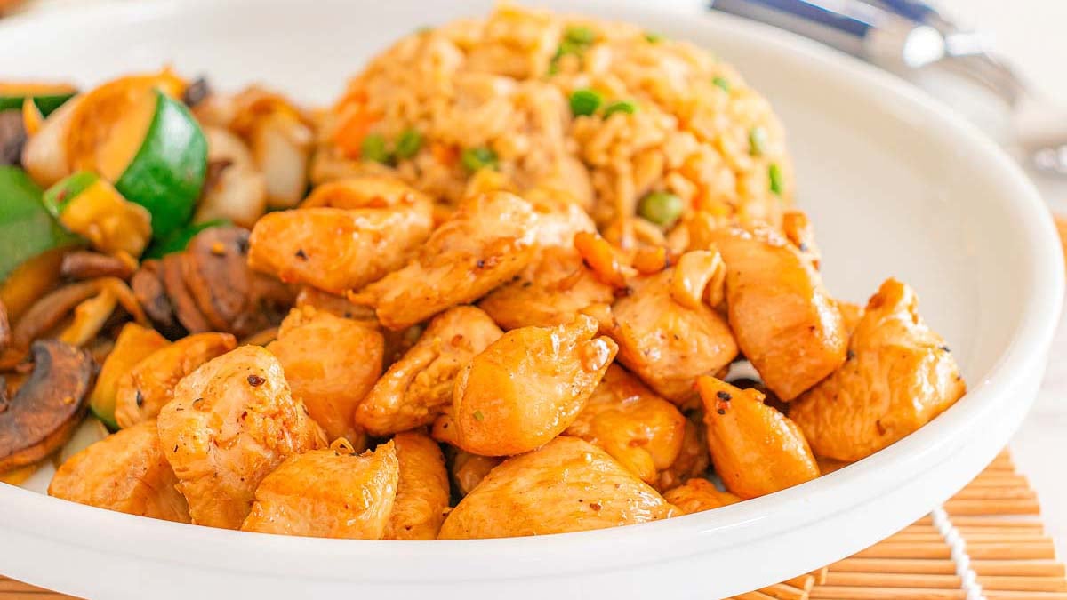 A plate of grilled chicken pieces, vegetable stir-fry, and fried rice served on a white dish.