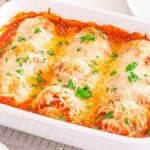 A white baking dish filled with a baked meatball casserole covered in tomato sauce and melted cheese sits on a cooling rack.
