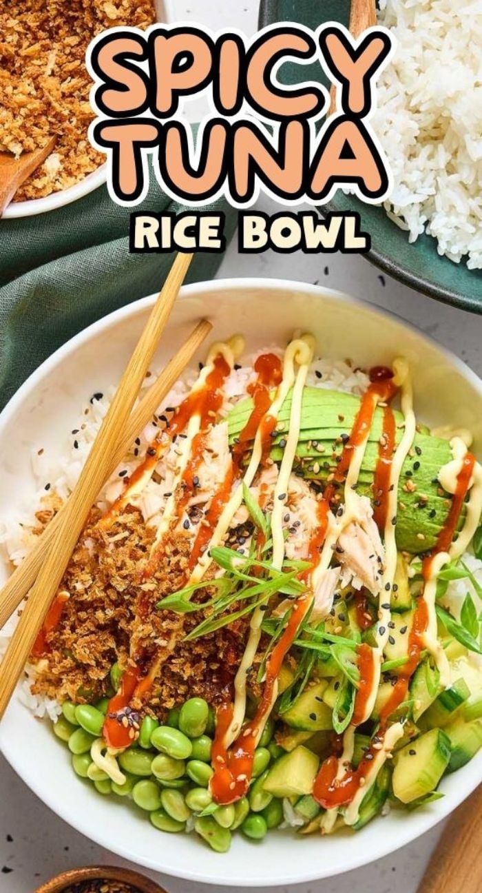 A flavorful spicy tuna rice bowl topped with creamy avocado, fresh edamame, vibrant sauce drizzles, and served with chopsticks on the side.