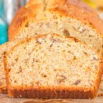 A sliced loaf of Bisquick banana bread, speckled with visible nuts, rests invitingly on a wooden board.
